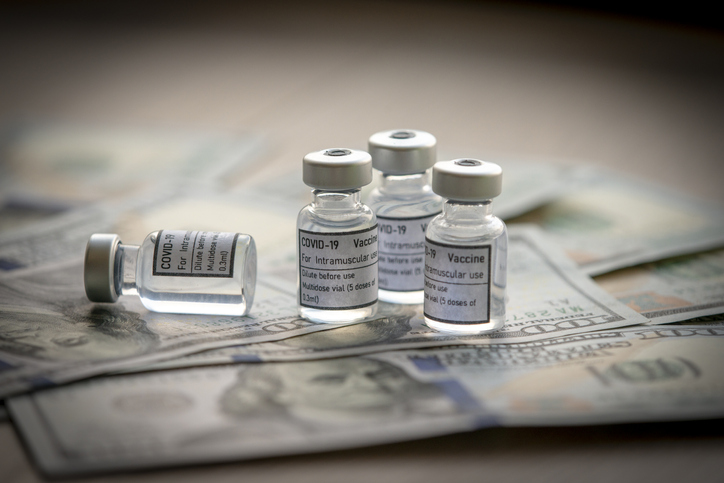 Covid-19 vaccine on a stack of US dollar and euro banknotes bills