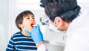 Male pediatrician examining little child patient’s throat at clinic