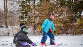 A boy teaches his little sister how to snowboard in winter