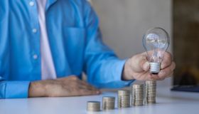 concept of savings or investment Businessman holding light bulb and pile of coins on table save energy and money concept with innovation and creative inspiration for saving energy