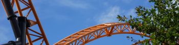 Orange-coloured roller coaster tracks of an extreme roller coaster, crossing under a blue sk